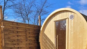 A wooden sauna structure with a door, a wooden fence, and a green artificial turf area.