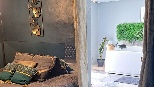 A bedroom with a bed, a wall-mounted decorative panel, and a view of a bathroom and outdoor area.