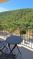 Un balcón con una mesa redonda y sillas, con vistas a una ladera boscosa.