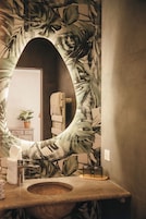 Un baño con un espejo grande, un lavabo, un perchero para toallas y una planta en maceta.