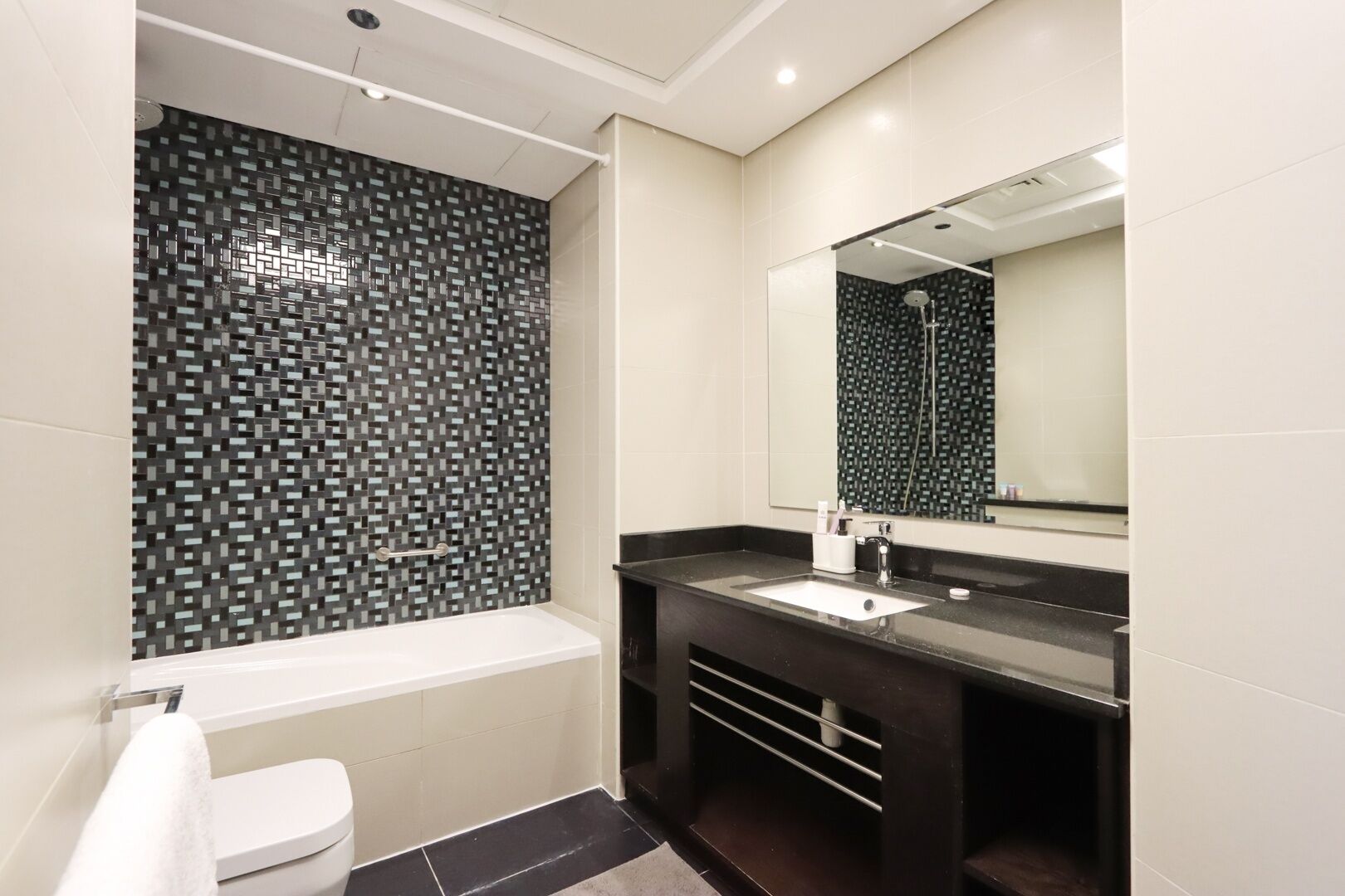A modern bathroom with a black and white mosaic backsplash, a white toilet, a black vanity with a sink, and a large mirror.