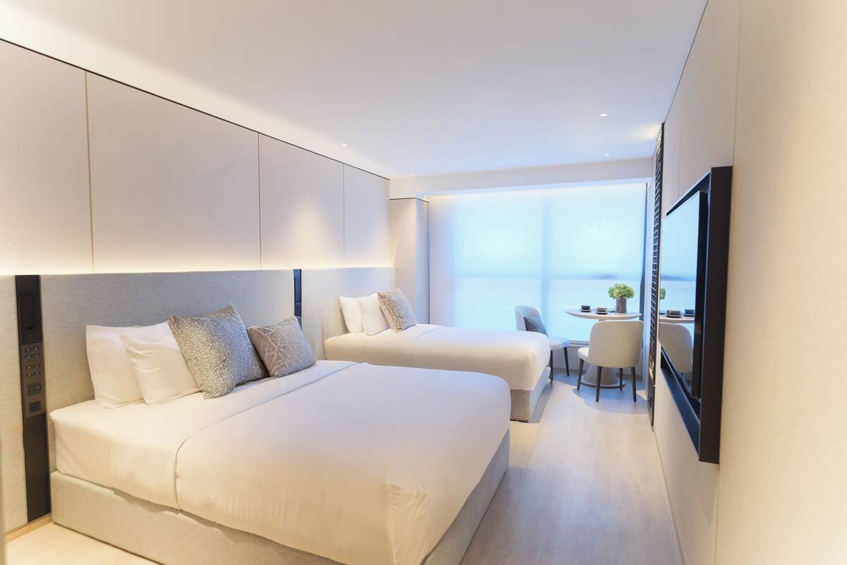 A modern hotel room with a large bed, a smaller bed, a desk, and a view of the city.