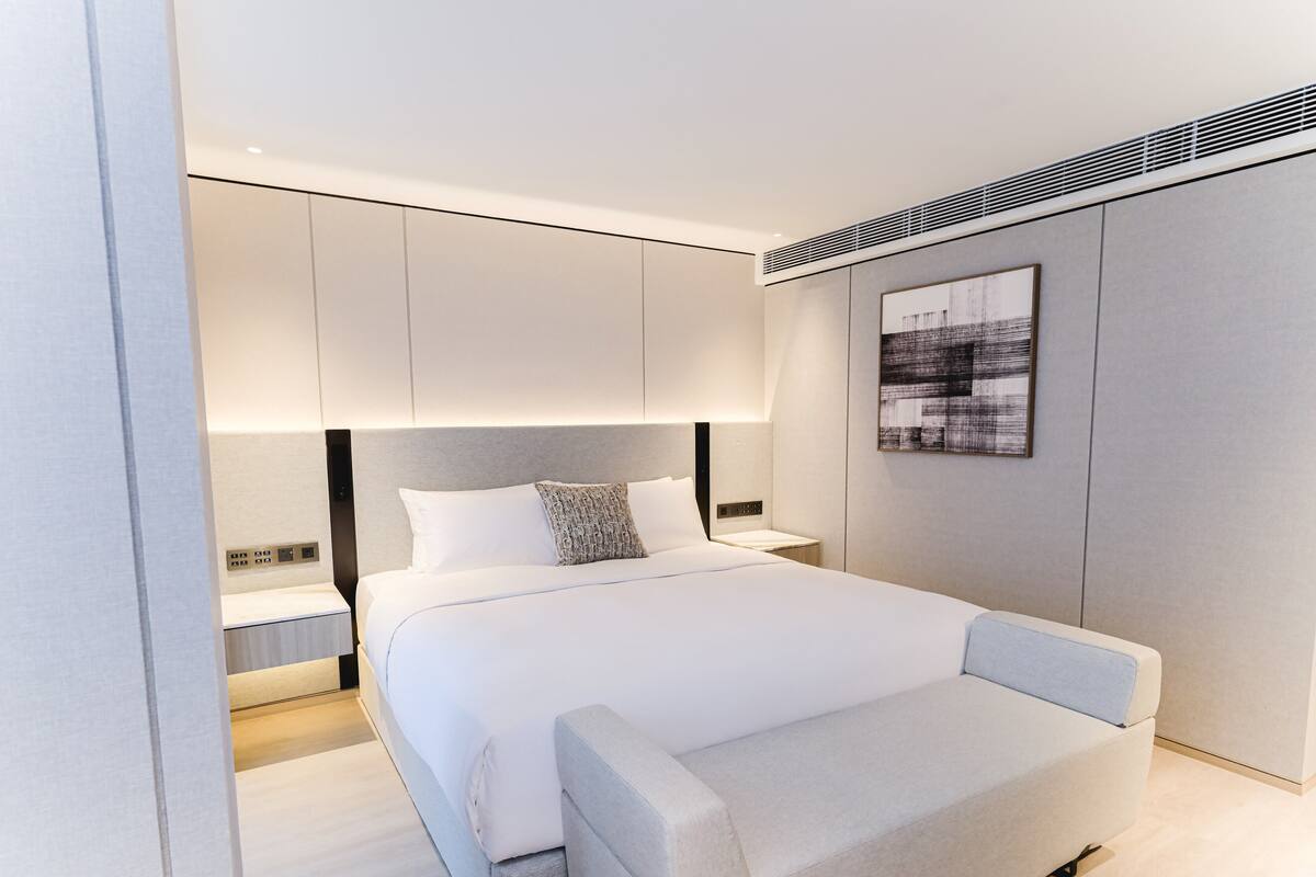 A modern bedroom with a large bed, a bedside table, a nightstand, and a wall-mounted artwork.