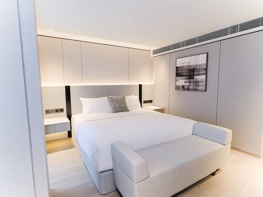 Une chambre moderne avec un grand lit, une table de chevet, une commode et une œuvre d’art accrochée au mur.