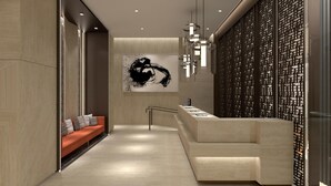En modern hotellobby med en receptionsdisk, en soffa med kuddar, en stor abstrakt målning och en dekorativ vägg med ett rutmönster.