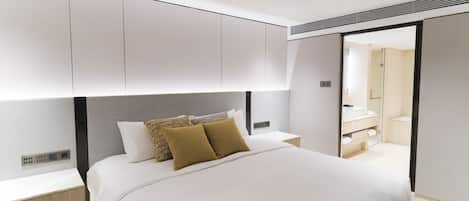 A modern hotel room with a large bed, built-in storage, and a bathroom visible through an open door.