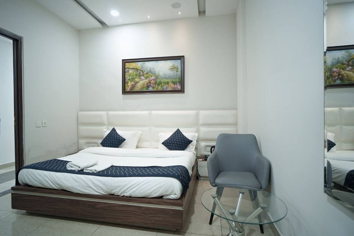 A modern bedroom with a large bed, a grey armchair, a glass coffee table, and a painting on the wall.