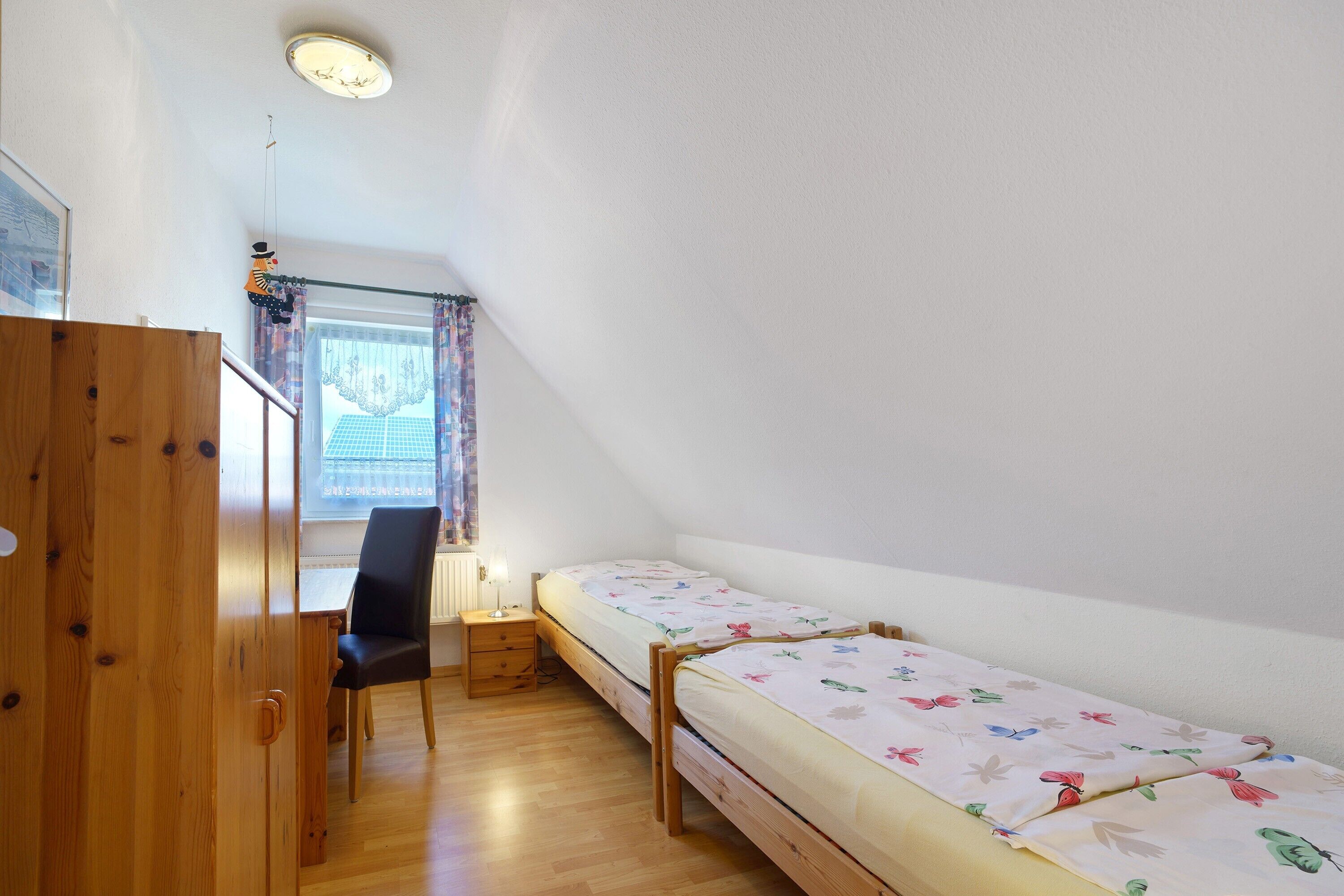 Ein kleines Zimmer mit Holztisch, Stuhl und zwei Einzelbetten.
