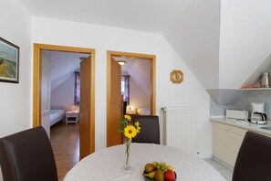 Een kleine kamer met een bed, een tafel met een bloevas en een keukenhoek met een koffiezetapparaat.
