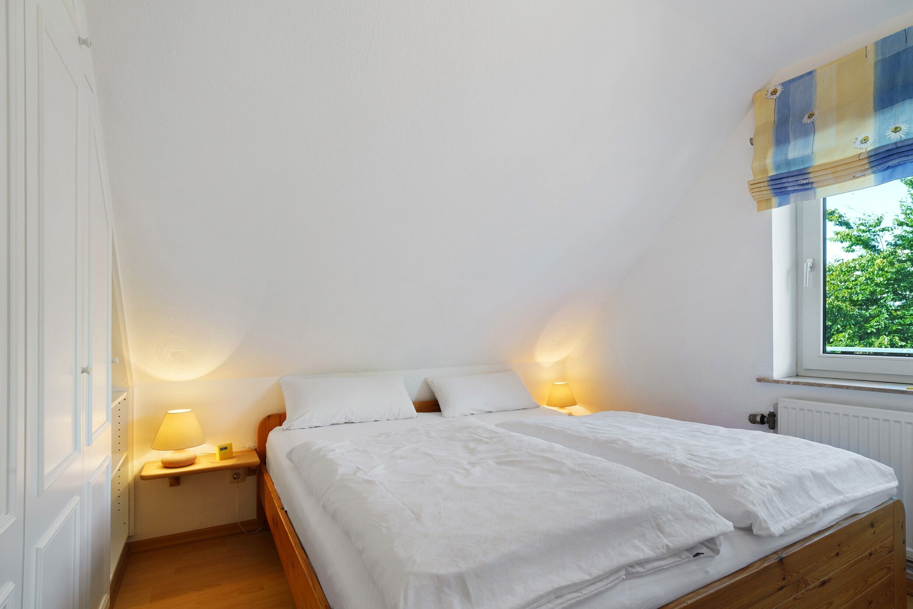 Une chambre à coucher avec un lit, des lampes de chevet, une fenêtre donnant sur un espace verdoyant et un radiateur.