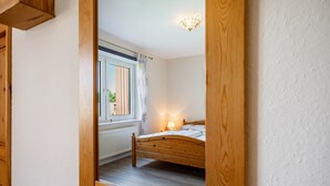 A bedroom with a wooden bed, a window with curtains, a radiator, and a ceiling light fixture. - Apartment '3' with Shared Terrace, Shared Garden and Wi-Fi (Nordstrand)