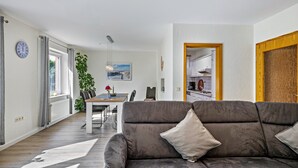 A modern living room with a grey sofa, a dining table, and a view into the kitchen. - Apartment '3' with Shared Terrace, Shared Garden and Wi-Fi (Nordstrand)