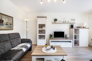 A modern living room with a sofa, coffee table, TV, shelves, and a painting. - Apartment '3' with Shared Terrace, Shared Garden and Wi-Fi (Nordstrand)