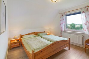 Un dormitorio con una cama de madera, dos mesitas de noche con lámparas, una ventana con cortinas y un radiador.