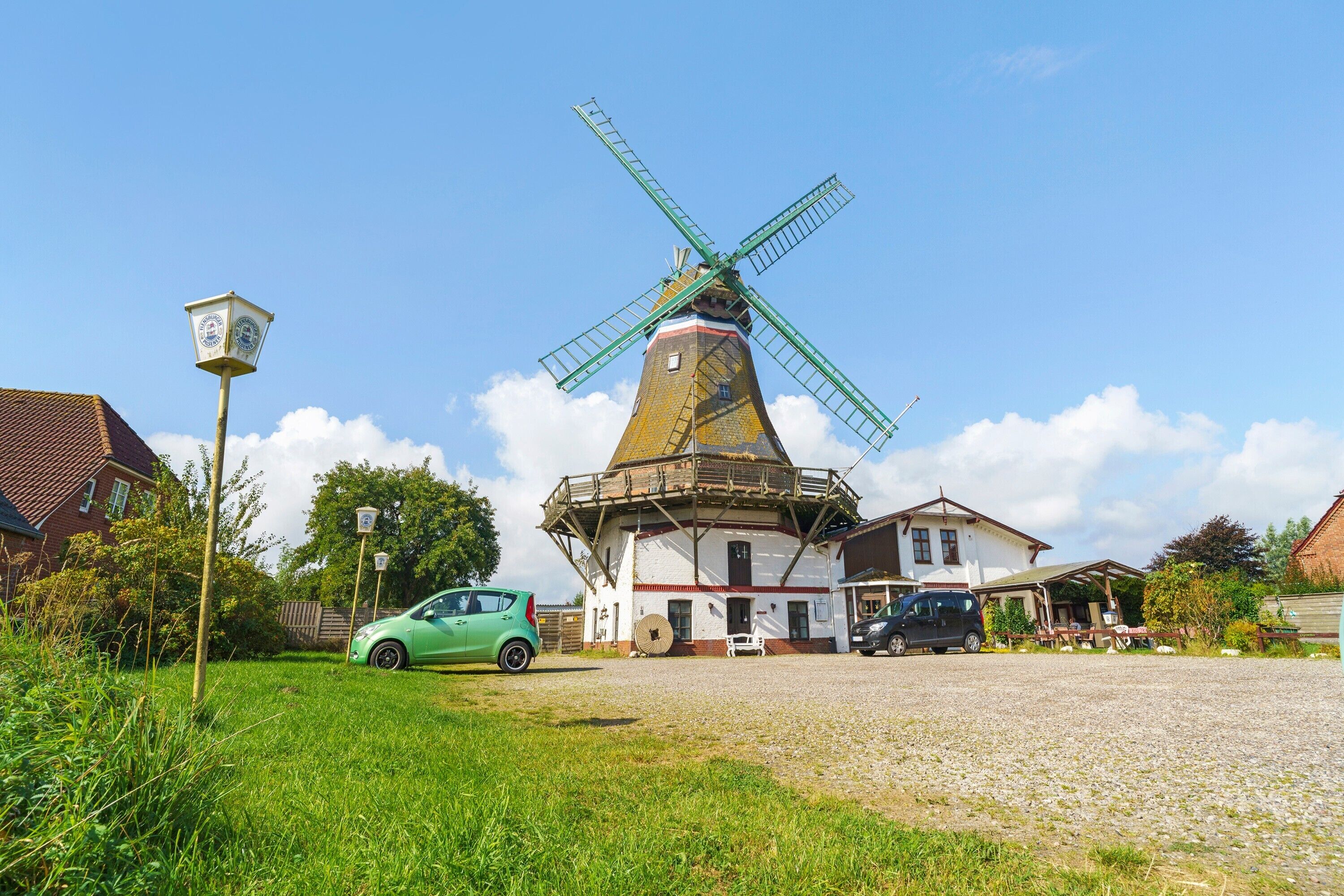 A windmill with a clock, surrounded by houses and a green car.
