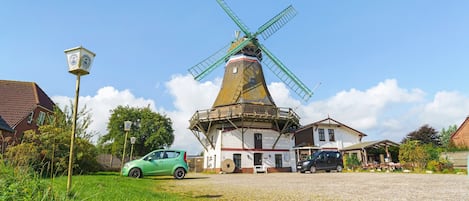 A windmill with a clock, surrounded by houses and a green car.