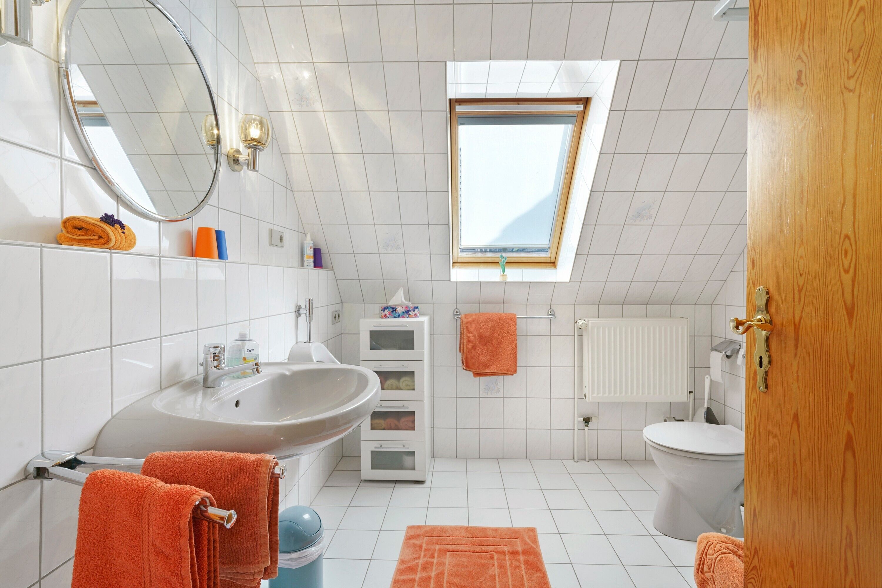 A bathroom with a skylight, white tiles, a sink, a toilet, and a mirror.
