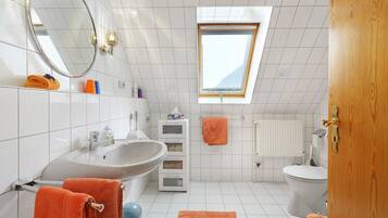 Et badeværelse med ovenlys, hvide fliser, en vask, et toilet og et spejl.