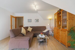 Een woonkamer met een bruine bank, een glazen salontafel, een houten kast en een lamp.