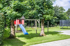 Een speeltuin met een glijbaan, schommels en een rode speelhoes.