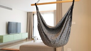 Una sala moderna con una silla hamaca colgante, un televisor de pantalla plana, un mueble verde claro y un sofá beige.