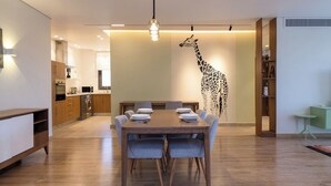 Un comedor moderno con una mesa y sillas de madera, un mural de jirafa en la pared y una cocina al fondo.