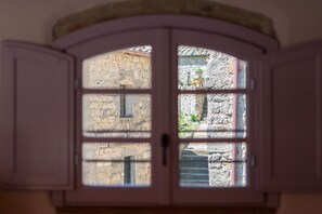 Une vue à travers une fenêtre, avec un mur de pierre et une porte au premier plan.