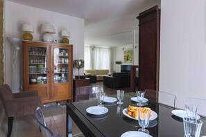 Un coin repas avec une table dressée pour quatre personnes, un buffet en bois doté de portes en verre, et un salon en arrière-plan.