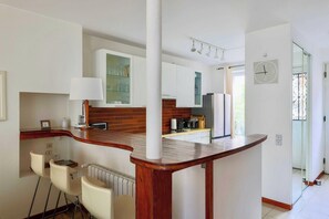 Une cuisine moderne avec des armoires blanches, un comptoir en bois et une cuisinière intégrée. On y trouve des tabourets de bar et une petite table à manger.