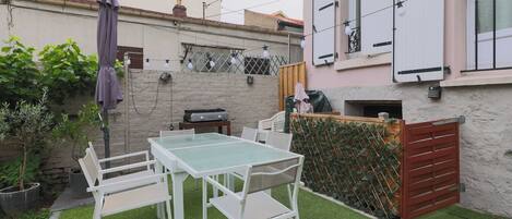 Un patio con mesa y sillas, una parrilla y un área cubierta con cerca.