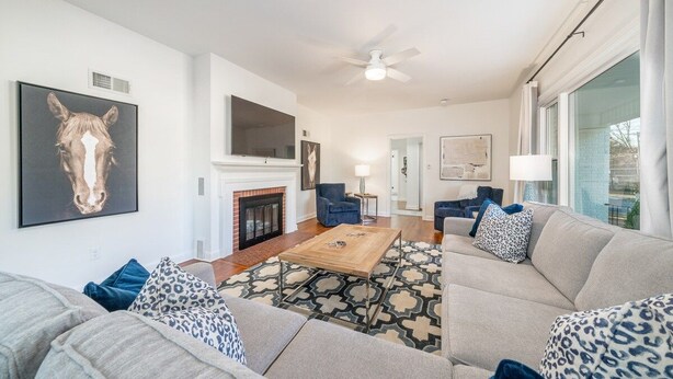 A modern living room with a fireplace, a ceiling fan, and a large window.