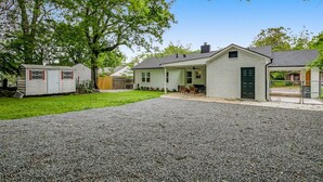 A residential property with a gravel driveway, a covered outdoor seating area, and a small shed.