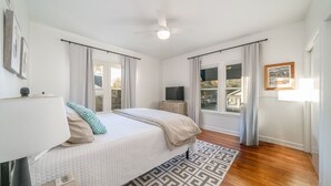 A bedroom with a bed, a television, a ceiling fan, and a window with curtains.