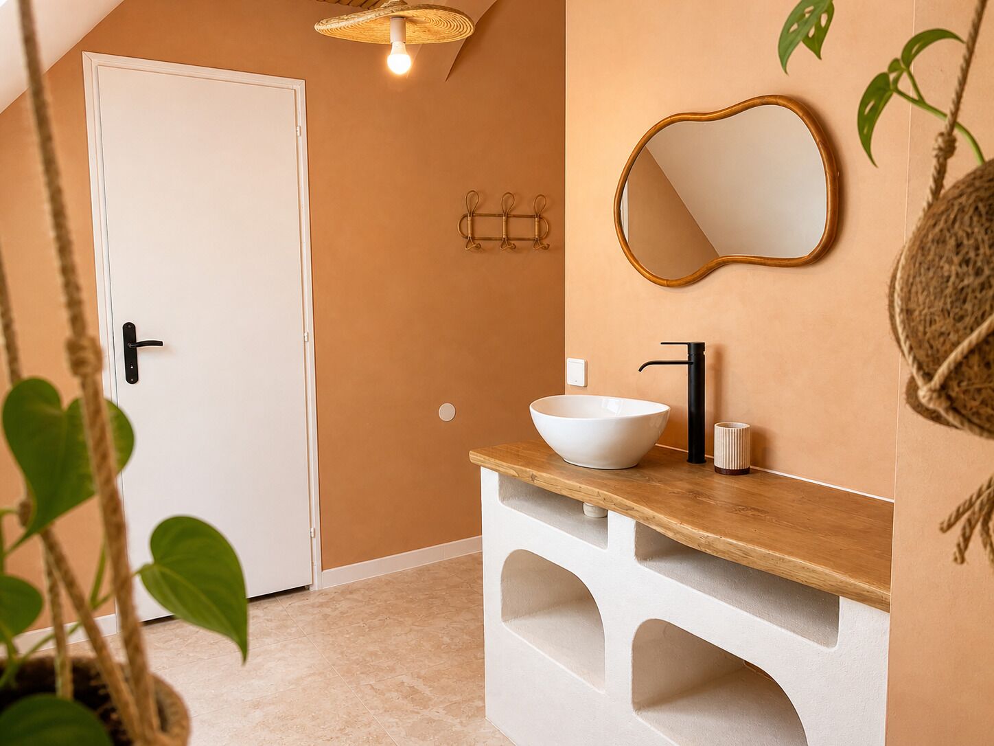 A bathroom with a white door, a white sink with a black faucet, a mirror with a gold frame, and a hanging plant.