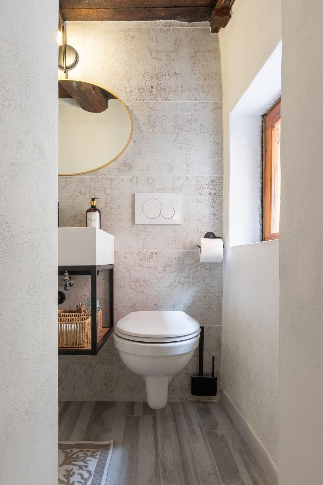 Une petite salle de bain avec des toilettes blanches, un distributeur de serviettes, un distributeur de savon liquide et un petit panier.