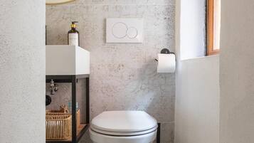 Une petite salle de bain avec des toilettes blanches, un distributeur de serviettes, un distributeur de savon liquide et un petit panier.