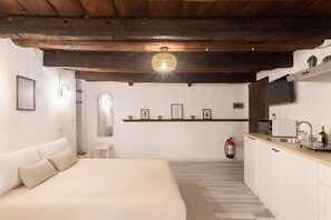 Ein Schlafzimmer mit einem Bett, einem kleinen weißen Hocker, einem Nachttisch, einem Spiegel und einem Regal mit gerahmten Bildern.