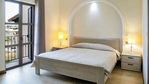 Une chambre à coucher comprenant un lit, deux tables de chevet avec des lampes, une grande fenêtre en arc de cercle et un balcon.