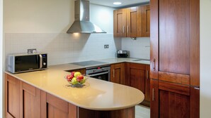 A kitchen with wooden cabinets, a microwave, a stove, and a fruit bowl on the counter. - 2 Bedroom Apartment - AHB11 (KOUKLIA)