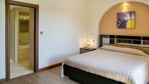 A bedroom with a bed, a nightstand, a wall-mounted painting, and a bathroom visible through an open door. - 2 Bedroom Apartment - AHB11 (KOUKLIA)