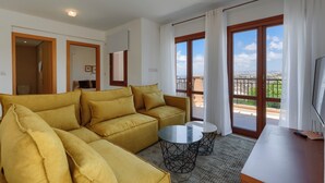 Een moderne woonkamer met een bank, een kleine tafel en een televisie. Er is een balkon met uitzicht.