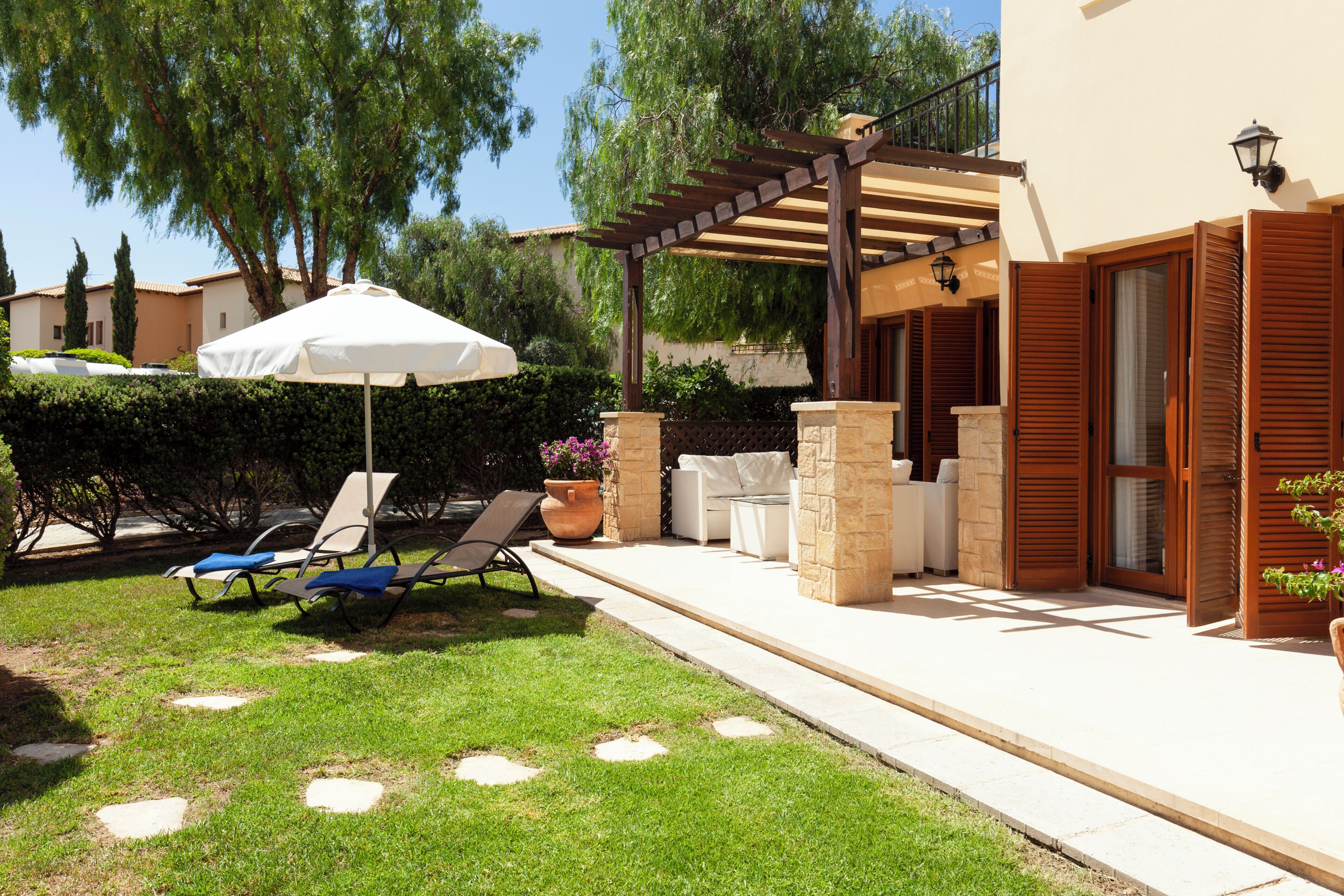 Un espace extérieur aménagé avec une pergola, des fauteuils de jardin et un parasol blanc.