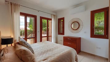 A bedroom with a bed, a dresser, a mirror, and a window with a view of greenery.
