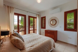 A bedroom with a bed, a dresser, a mirror, and a window with a view of greenery. - 2 Bedroom Apartment - BE02 (kouklia)