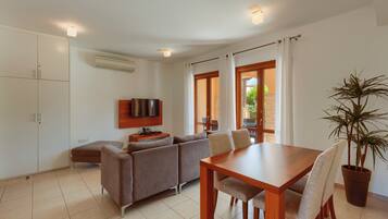 A modern living room with a sofa, a wooden dining table, and a television.