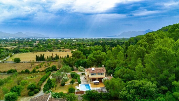 Une maison avec une piscine, entourée d’une végétation luxuriante et dominée par un paysage montagneux.