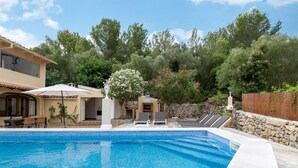 Une piscine avec des chaises longues, un espace patio et un mur en pierre.