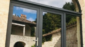 A large arched window with a sliding door, revealing a stone building with a tiled roof and a chimney. - Domaine de Péroline: Swimming pool and Jacuzzi (Cézac)
