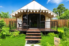 A tent-like structure with a covered entrance, a small outdoor seating area with chairs, and a paved pathway leading to the entrance.