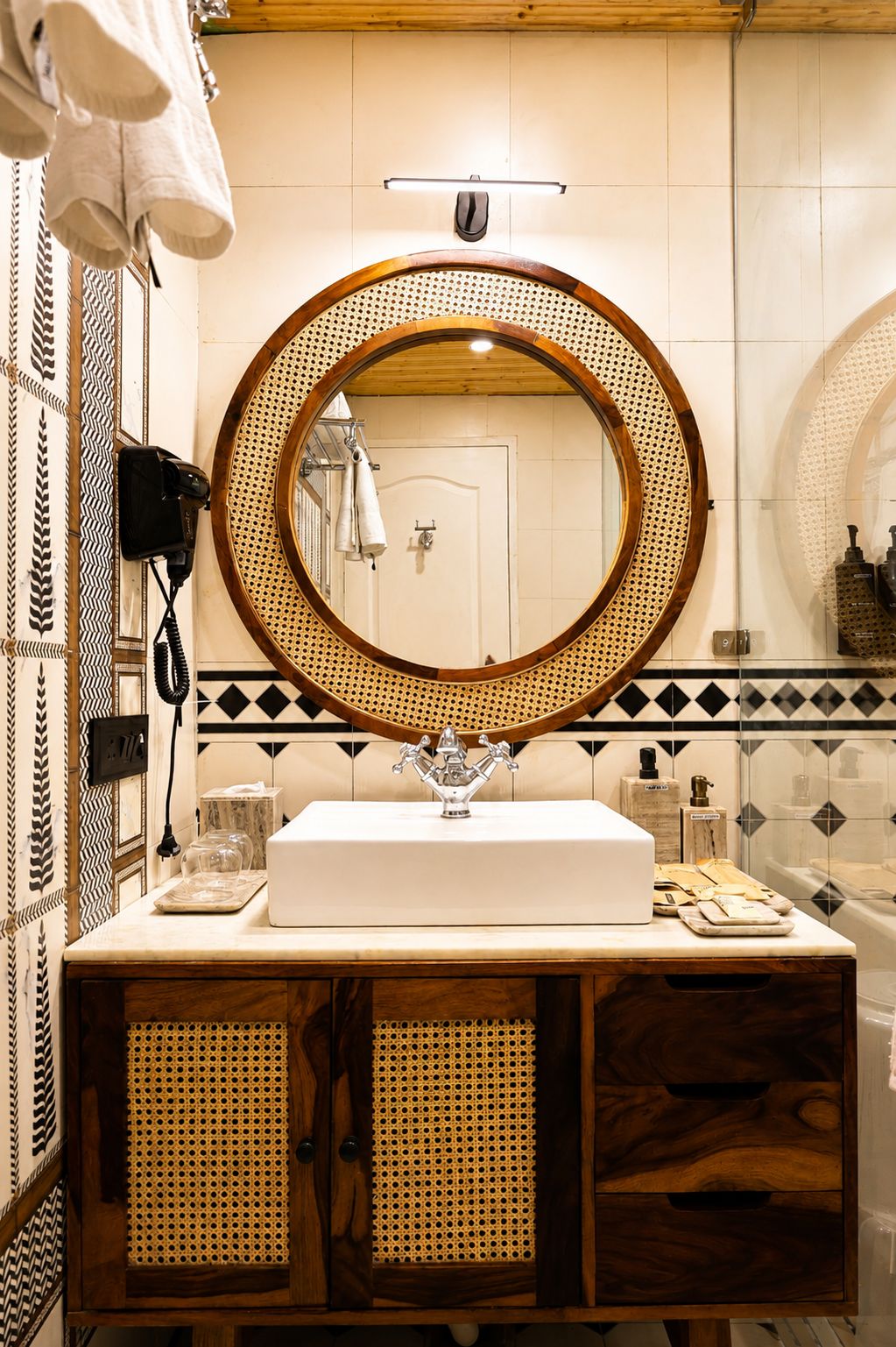 A bathroom with a round mirror, white sink, and wooden cabinet with a woven front panel.